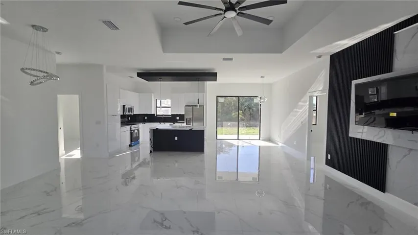 Kitchen featuring open floor plan, hanging light fixtures, a center island with sink, light marble finish flooring, and stainless steel appliances