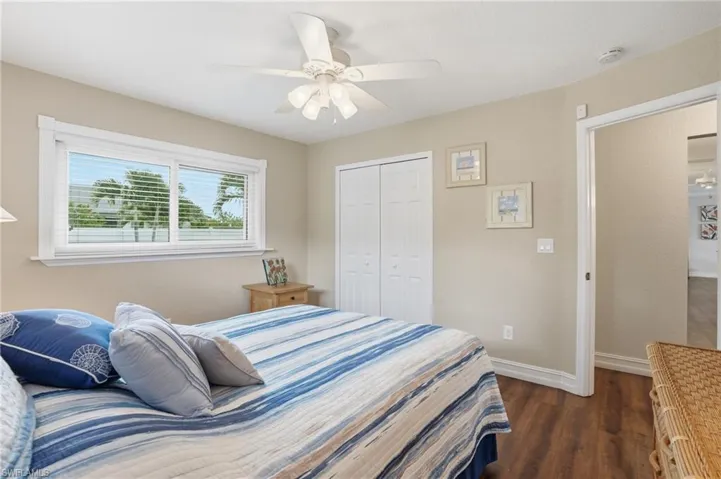 Bedroom featuring wood-finish flooring, a double window with blinds, a ceiling fan with light fixture, and bifold closet doors