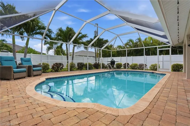 Screened swimming pool area featuring a curved pool with tiled steps, surrounding paver patio, white privacy fencing, and tropical landscaping