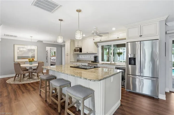 Spacious kitchen featuring a large island with granite countertops, wood-finish flooring, white cabinetry, and stainless steel appliances