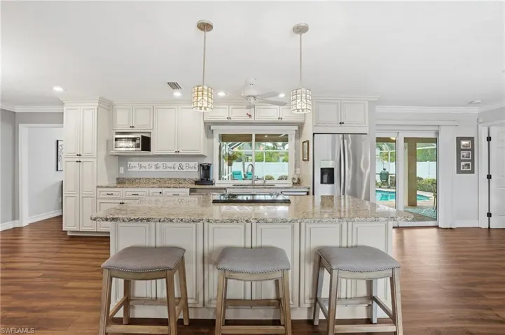 Spacious kitchen featuring an expansive island with granite countertop, white paneled cabinetry, stainless steel appliances, and wood-finish flooring