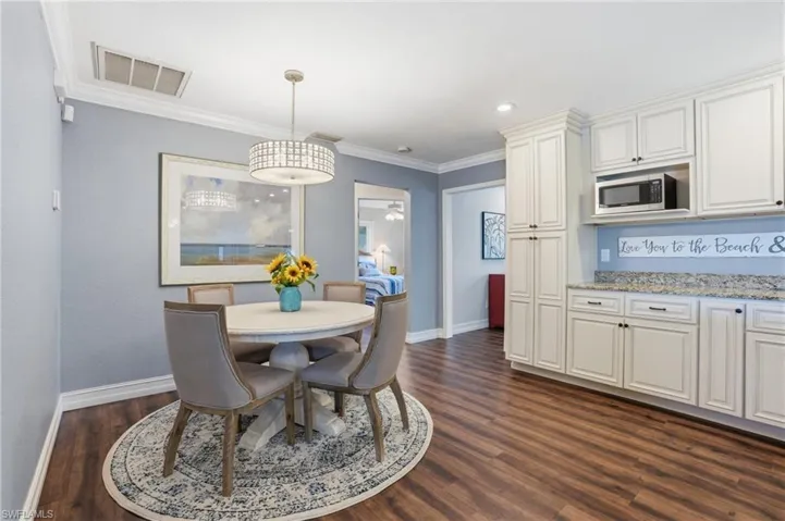 Eat-in kitchen featuring wood-finish flooring, white cabinetry with dark hardware, a built-in microwave, and granite-style countertops