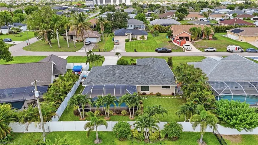 Aerial perspective showcasing a single-story residence with a gray shingle roof and a screened-in pool enclosure