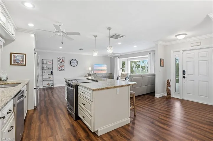 Open-concept living space featuring wood-finish flooring, a kitchen island with stone countertops, white cabinetry, and recessed lighting