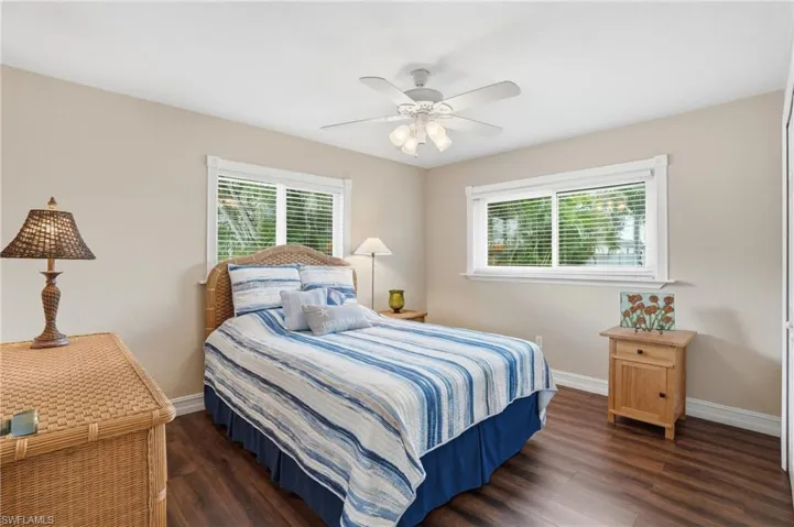 Bedroom featuring two windows with white blinds, wood-finish flooring, and a ceiling fan with integrated lighting
