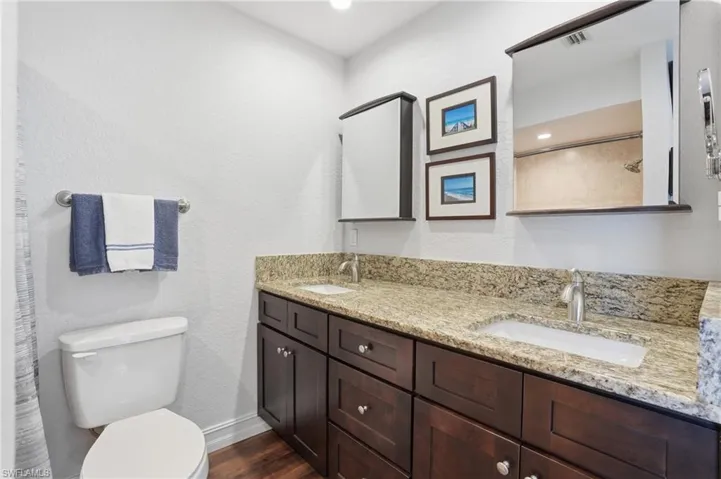Dual vanity featuring a granite countertop with two undermount sinks, brushed nickel faucets, and rich wood-finish cabinetry