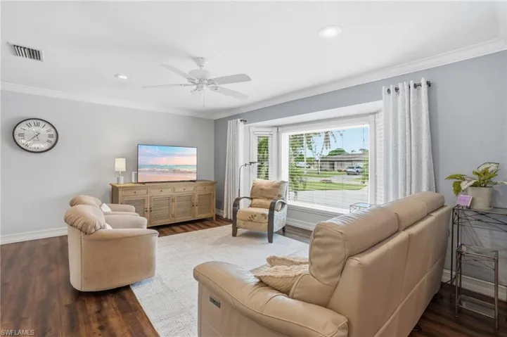 Bright living space featuring a bay window, wood-finish flooring, recessed lighting, crown molding, and a ceiling fan