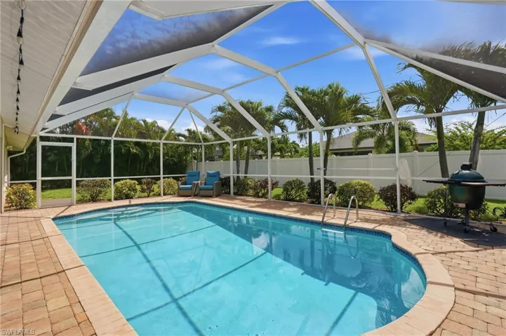 Screened-in swimming pool featuring brick paver decking, a curved pool design, integrated pool steps, and a white privacy fence