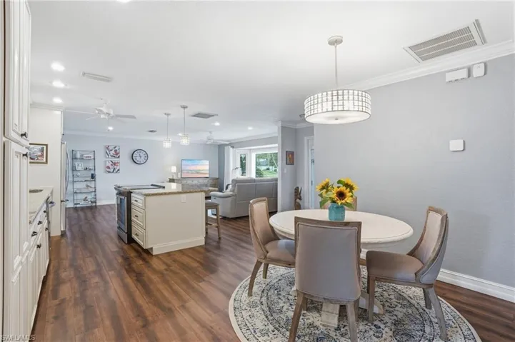 Open-concept interior featuring wood-finish flooring, a kitchen island with stone countertops, recessed lighting, and crown molding
