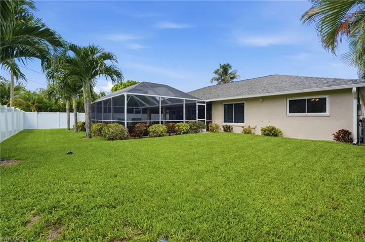 Spacious rear yard featuring a screened enclosure, mature palm trees, a well-maintained lawn, privacy fencing, and established perimeter landscaping