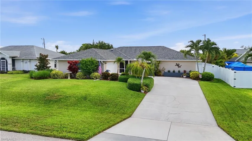 Single-story residence featuring a paved driveway, mature landscaping, and a shingled roof