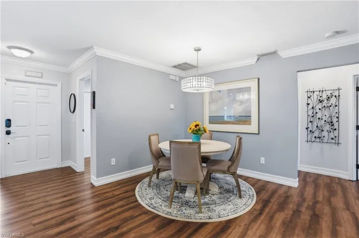 Dining area featuring wood-finish flooring, a contemporary chandelier, and light gray walls with white crown molding