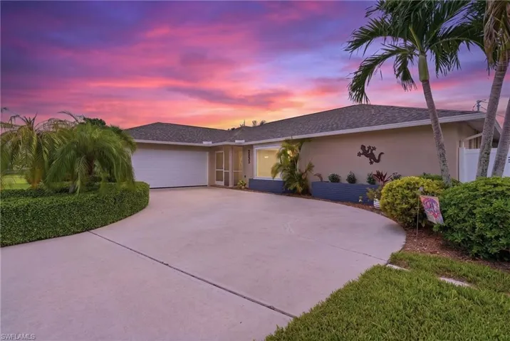 Exterior stucco residence with a two-car garage, mature palm trees, and lush landscaping