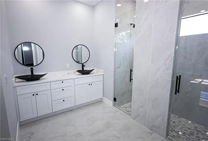 Bathroom with double vanity, a sink, marble finish floor, and a shower stall