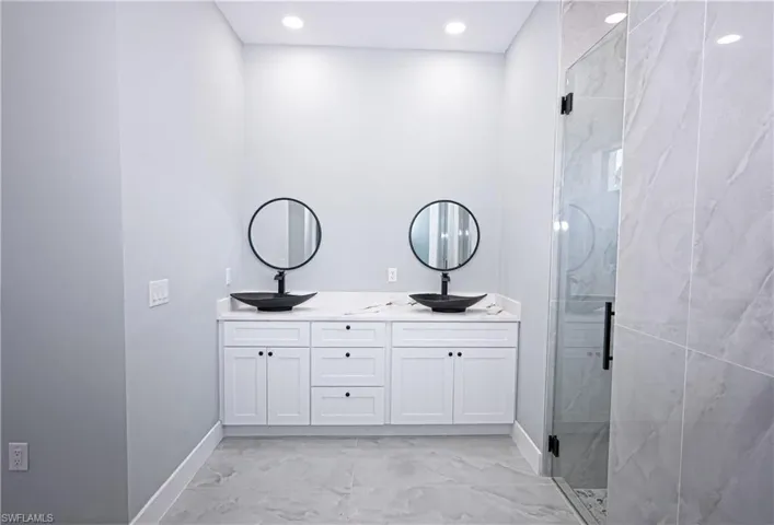 Bathroom with double vanity, marble finish floor, baseboards, a sink, and a marble finish shower