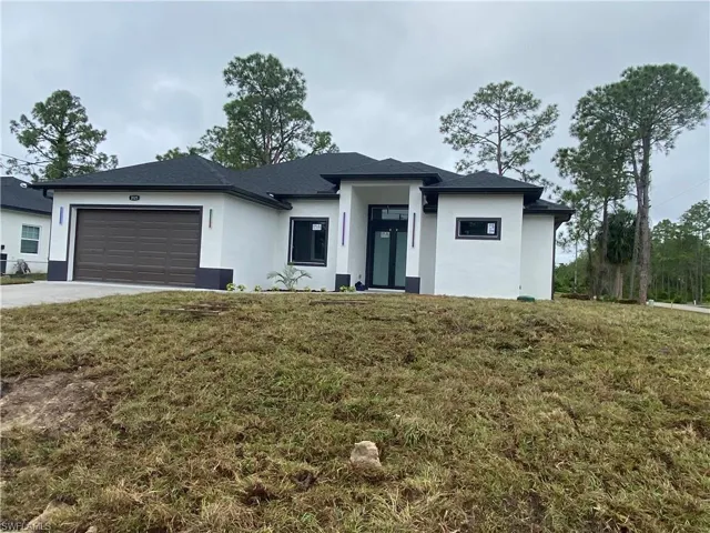 View of front of property with a front yard, driveway, stucco siding, and an attached garage