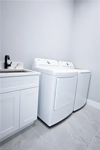 Washroom with cabinet space, a sink, separate washer and dryer, marble finish floor, and baseboards