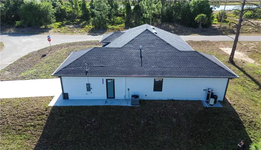 Back of house with a lawn, roof with shingles, and central AC