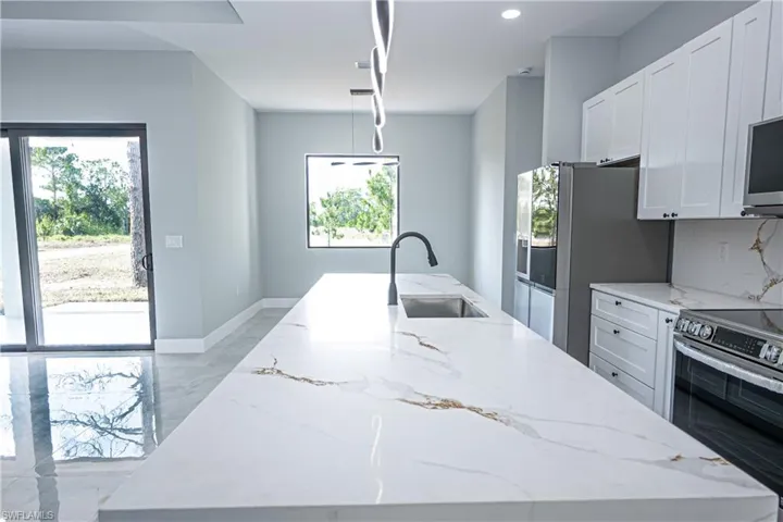 Kitchen with marble finish floor, an island with sink, light stone counters, a sink, and stainless steel appliances
