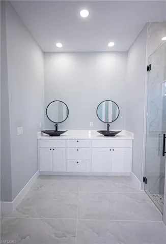 Bathroom featuring baseboards, double vanity, marble finish floor, and a marble finish shower