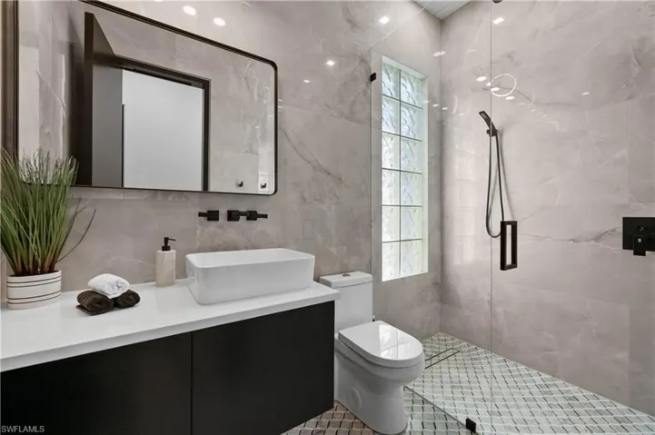 Bathroom featuring tile walls, backsplash, walk in shower, vanity, and toilet
