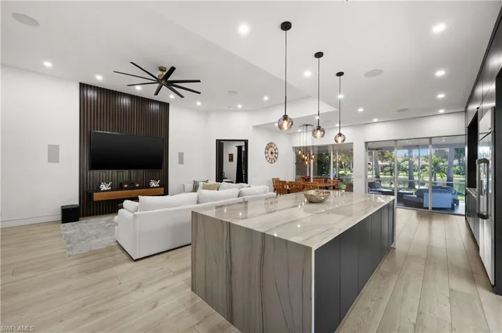 Kitchen with ceiling fan, light stone counters, hanging light fixtures, a large island, and light wood-type flooring