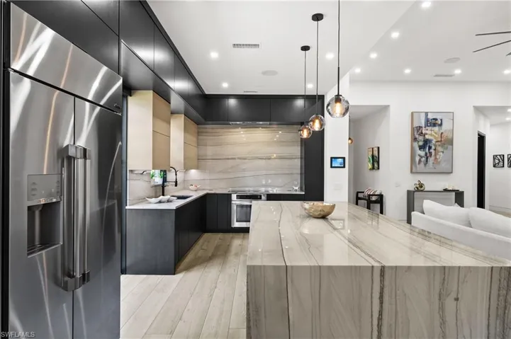 Kitchen with hanging light fixtures, sink, a large island, stainless steel appliances, and light hardwood / wood-style floors