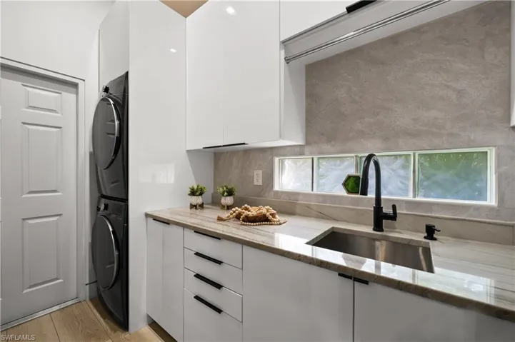 Kitchen featuring white cabinets, sink, stacked washer and dryer, light stone countertops, and light hardwood / wood-style floors