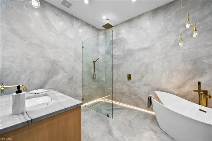 Bathroom featuring independent shower and bath, vanity, and tile walls