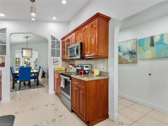 Kitchen with arched walkways, pendant lighting, appliances with stainless steel finishes, light tile patterned floors, and light stone countertops