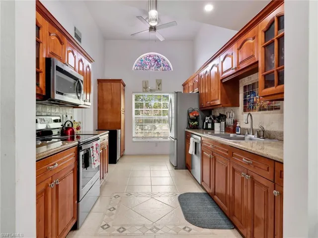 Kitchen featuring stainless steel appliances, light stone countertops, ceiling fan, and glass insert cabinets