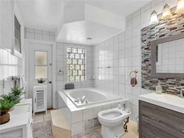 Bathroom featuring tile walls, vanity, a bath, a bidet, and light tile patterned floors