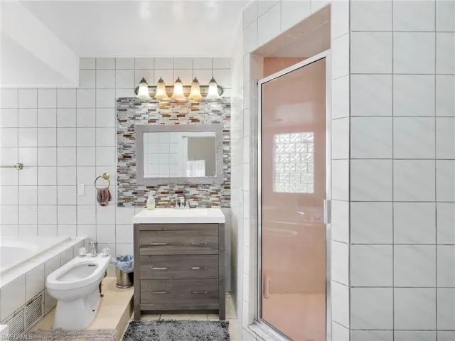 Full bath featuring vanity, a bidet, tile walls, a shower stall, and a bath