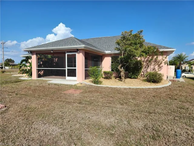 Back of house featuring a lawn, a sunroom, a shingled roof, and stucco siding.  Well located at back of house