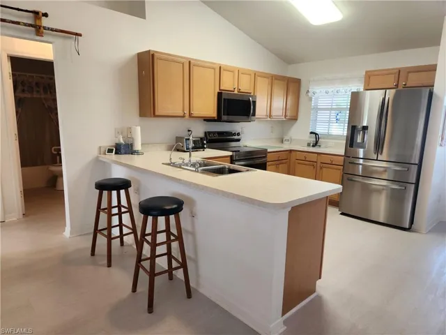 Kitchen featuring stainless steel appliances, a peninsula, light countertops, a kitchen bar, and lofted ceiling