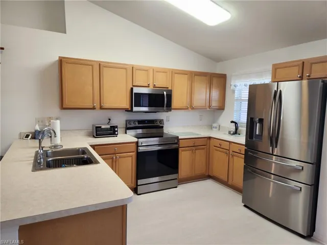 Kitchen with stainless steel appliances, light countertops, vaulted ceiling, a peninsula, and wood finish cabinets
