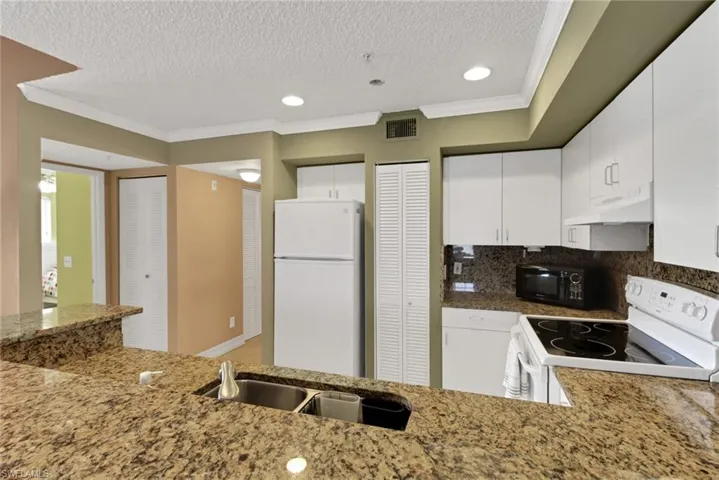 Kitchen with ornamental molding, white appliances, white cabinetry, a textured ceiling, and decorative backsplash