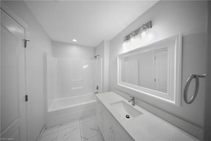 Bathroom with vanity, tub / shower combination, light marble finish floors, and recessed lighting