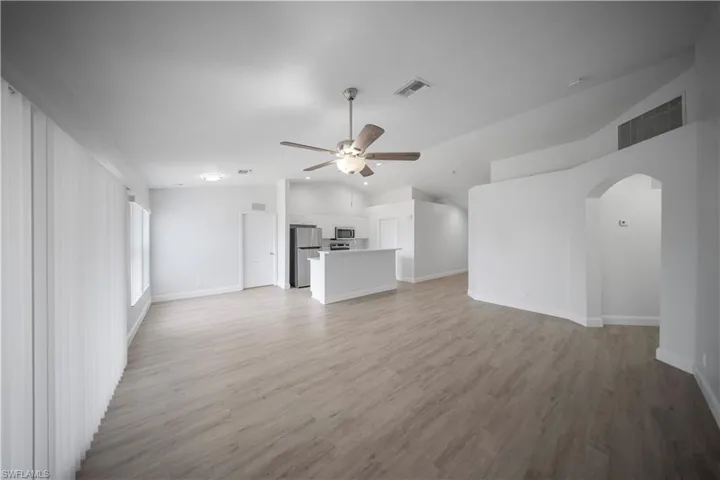 Unfurnished living room featuring lofted ceiling, light wood finished floors, arched walkways, and a ceiling fan