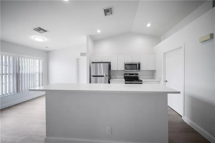 Kitchen with appliances with stainless steel finishes, vaulted ceiling, white cabinetry, a center island, and light stone counters
