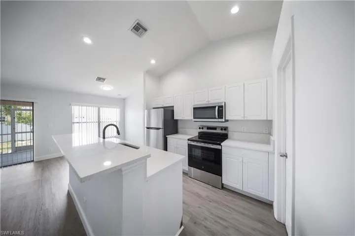 Kitchen with appliances with stainless steel finishes, an island with sink, white cabinetry, recessed lighting, and light wood-type flooring