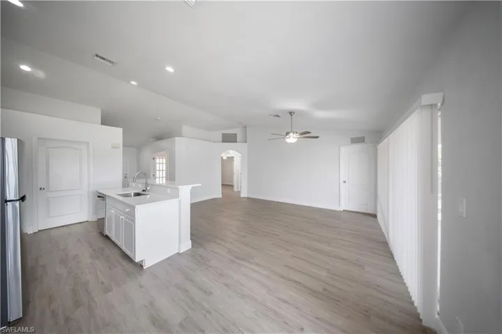 Kitchen featuring lofted ceiling, arched walkways, an island with sink, stainless steel appliances, and light wood-type flooring