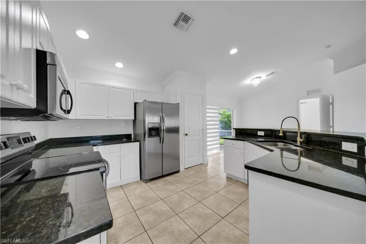 Kitchen with appliances with stainless steel finishes, white cabinets, crown molding, light tile patterned floors, and recessed lighting