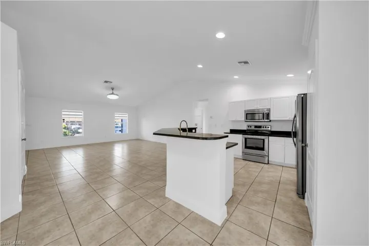 Kitchen with stainless steel appliances, dark countertops, light tile patterned floors, white cabinetry, and lofted ceiling
