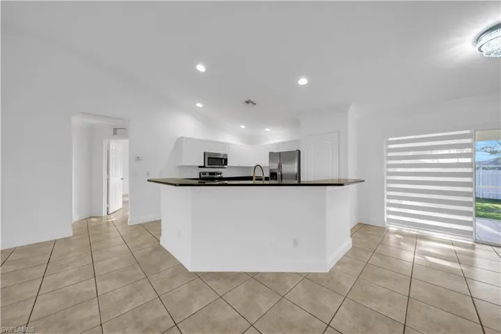 Kitchen with stainless steel appliances, dark countertops, white cabinets, vaulted ceiling, and crown molding