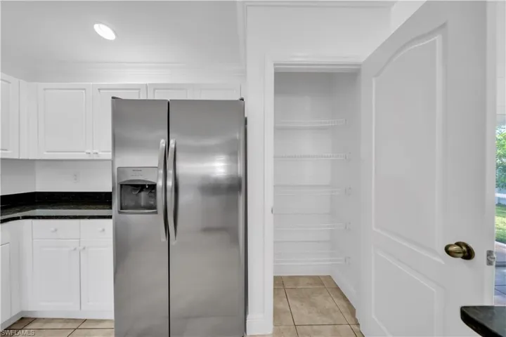 Kitchen with stainless steel fridge with ice dispenser, white cabinetry, light tile patterned floors, and dark stone countertops