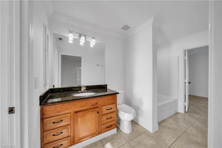 Bathroom featuring tile patterned flooring, vanity, crown molding, and a tub to relax in