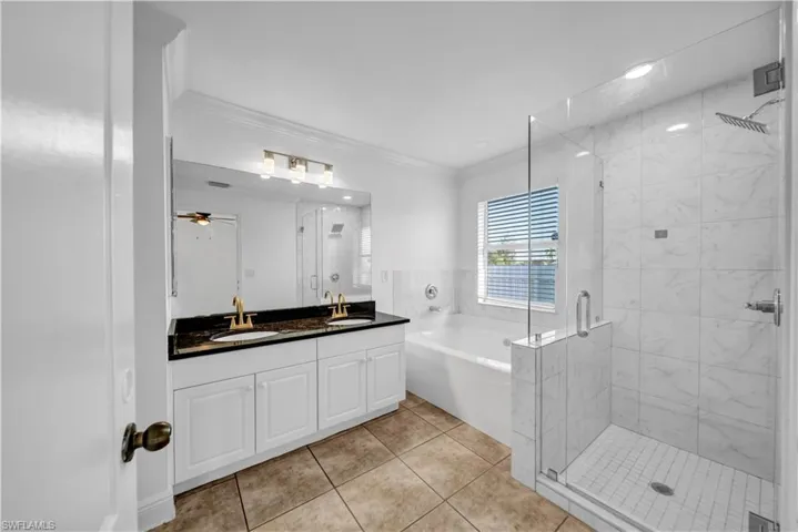 Full bath featuring a garden tub, ornamental molding, double vanity, a shower stall, and tile patterned flooring