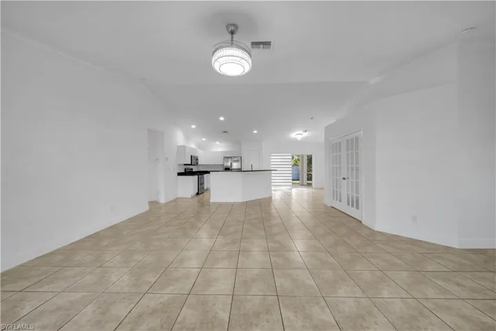 Unfurnished living room with vaulted ceiling, light tile patterned flooring, recessed lighting, and french doors