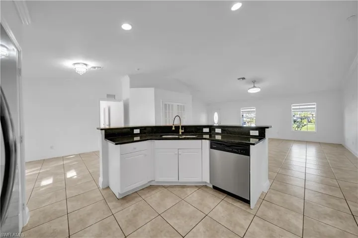 Kitchen featuring dishwasher, light tile patterned flooring, lofted ceiling, open floor plan, and white cabinetry